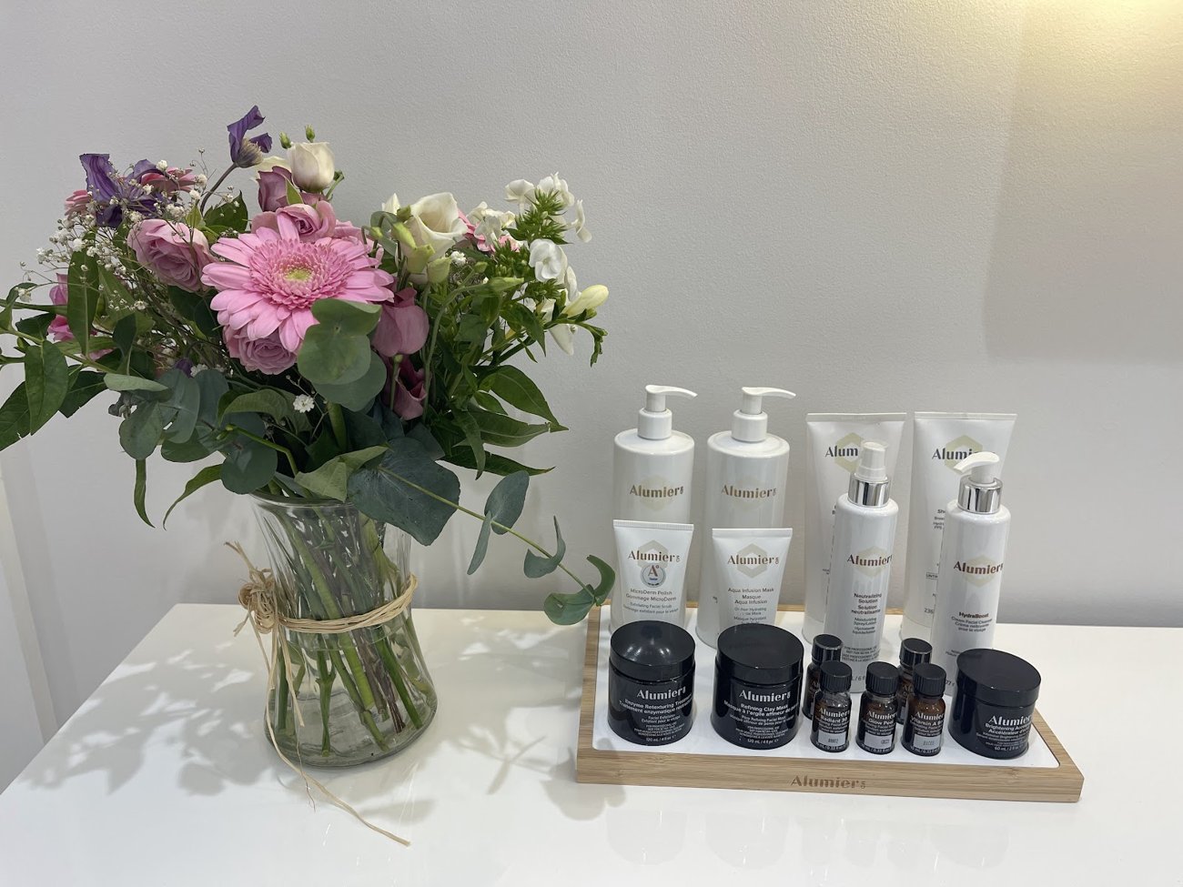 Medical-grade AlumierMD skincare and fresh flowers on a clean clinic surface.